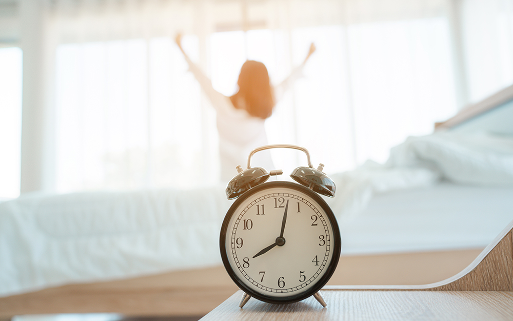 Alarm clock with woman stretching by bed.