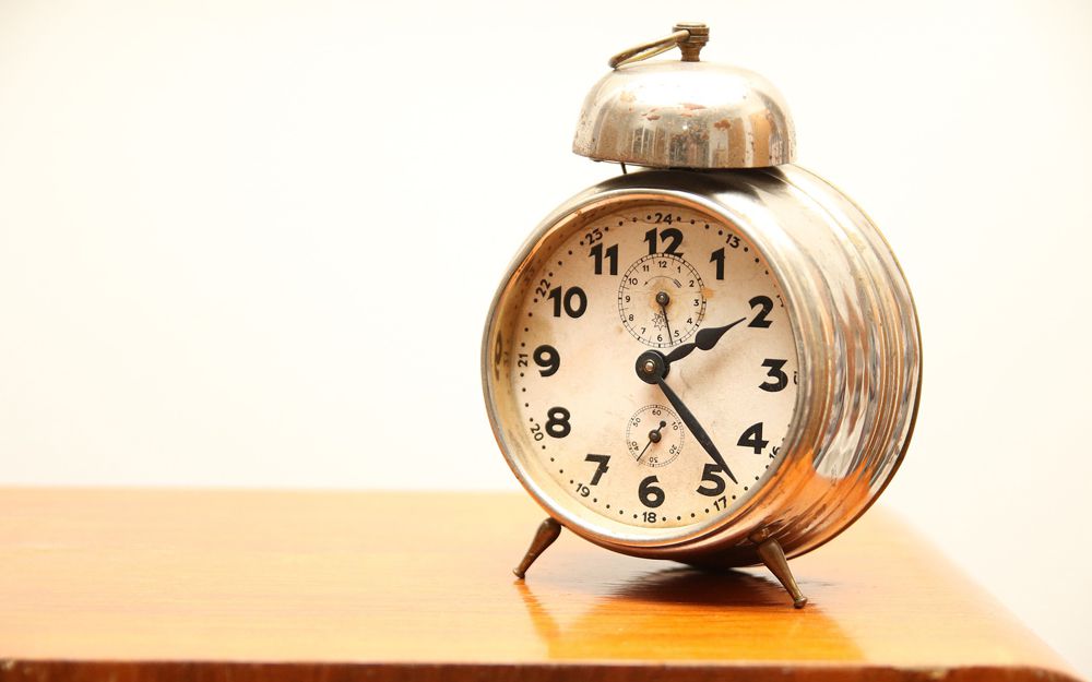 A traditional alarm clock on a bedside table, a helpful way to stick to a good sleep routine