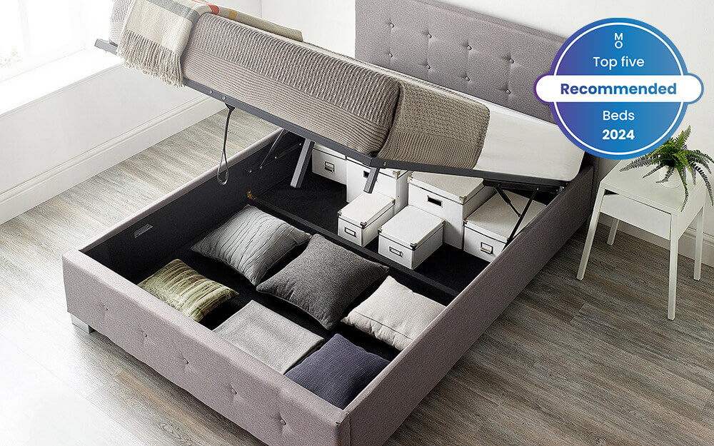 Image of the Aspire Ottoman Storage Bed with the storage space lifted open showing multiple boxes and pillows fitting within the storage space. Included in the image is a badge overlay stating that this mattress is one of Mattress Online's top five recommended beds of 2024.