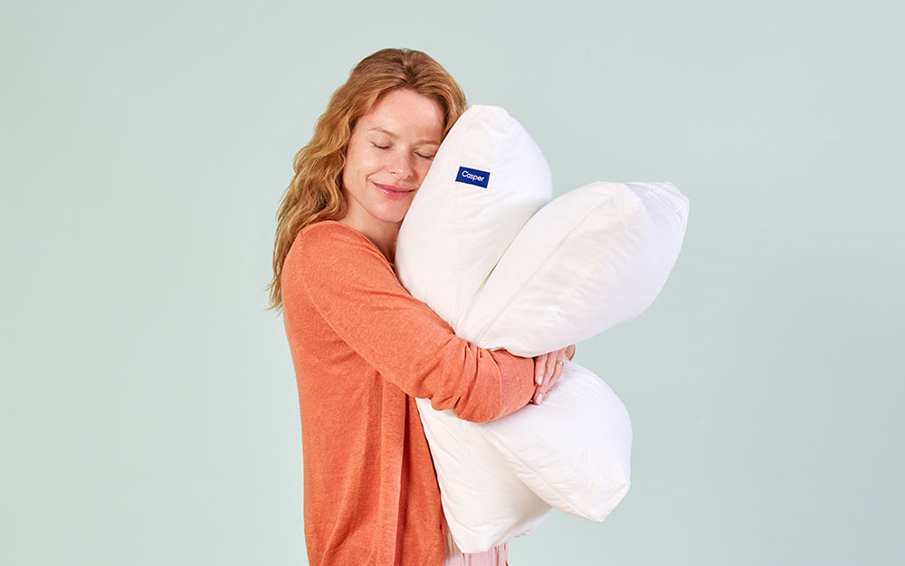 A woman hugging two Casper Pillows against a teal background.