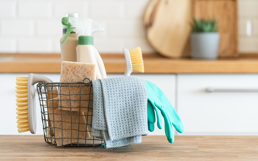 A basket of cleaning supplies on a wooden kitchen counter.