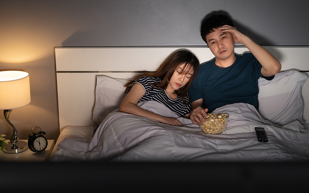 Couple falling asleep while watching TV in bed and eating popcorn