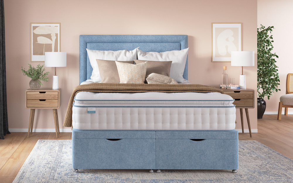 The Dunlopillo Elite Comfort 1400 Pocket Pillow Top Mattress in a pale pink bedroom on a blue fabric divan bed.