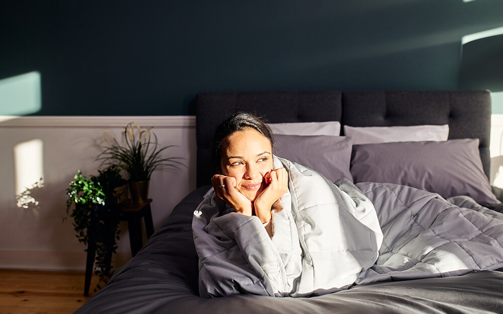 A woman wrapped up in the Emma Hug Weighted Blanket smiling.