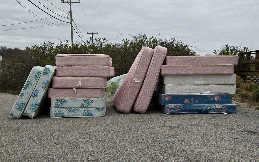 Piles of mattresses that have been fly tipped next to a field.