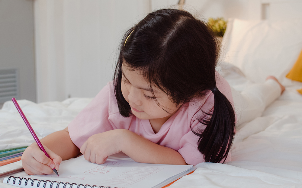 Young girl drawing in bed