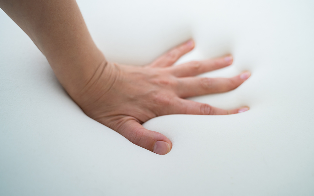 A hand pressing into a memory foam mattress