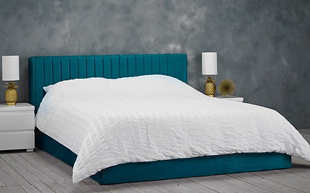 A teal coloured LPD Berlin Velvet Ottoman Bed Frame in a grey bedroom.