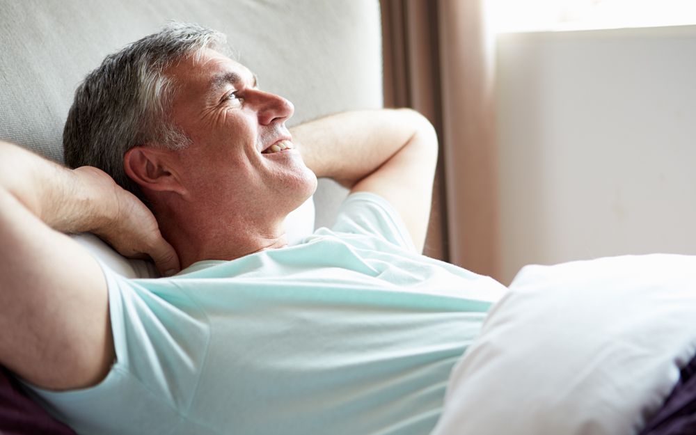 A man lying back in bed, happy and without a bad back thanks to the support of a comfortable orthopaedic mattress