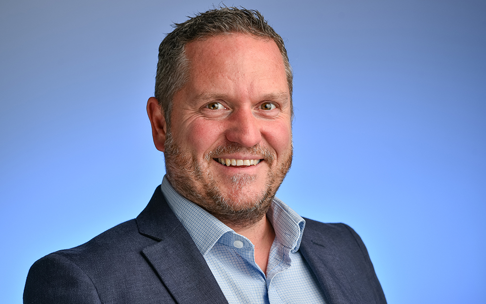 Martin Eastwood, Chief Operating Officer, standing in front of a blue background smiling.