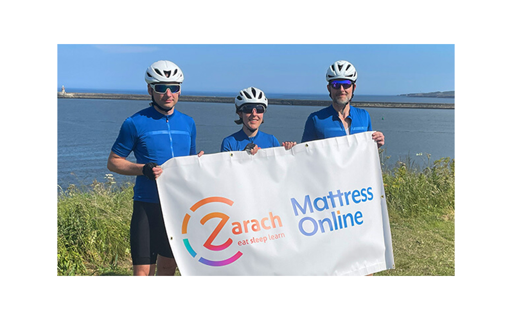 Three members of the Mattress Online team holding a banner that for Zarach after completing the coast to coast