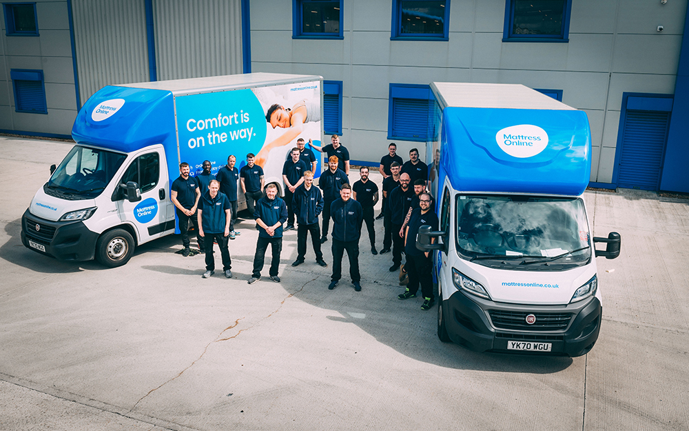 A group of Mattress Online staff standing between two delivery vans