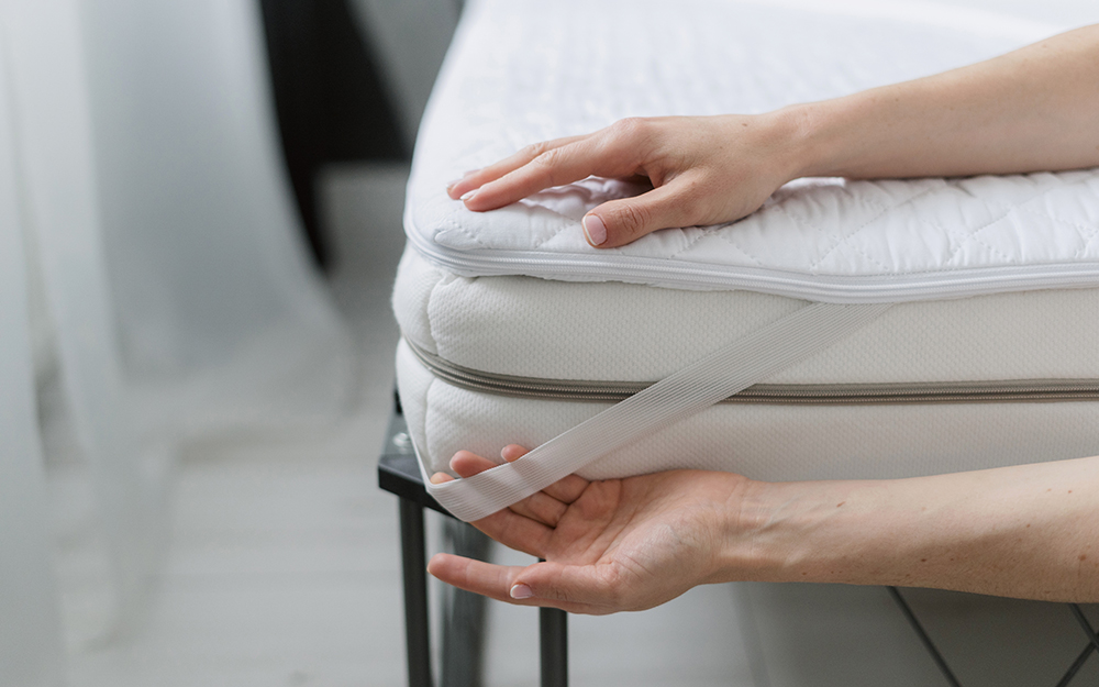 A person attaching a mattress topper to a mattress