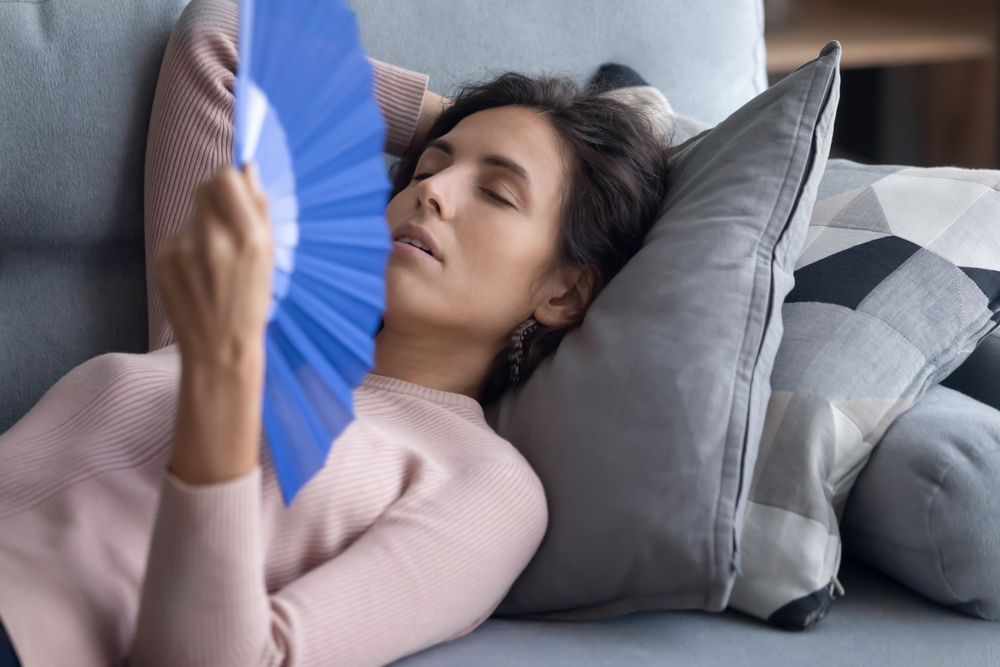 Woman trying to sleep on sofa cushion with blue fan