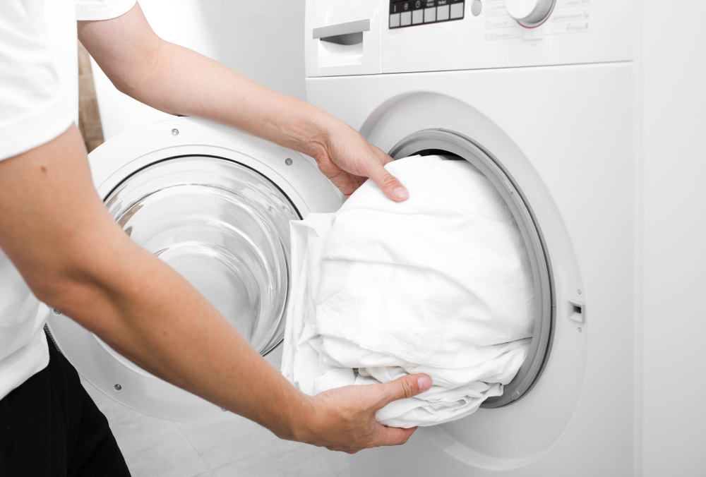 Person putting white bedding into washing machine