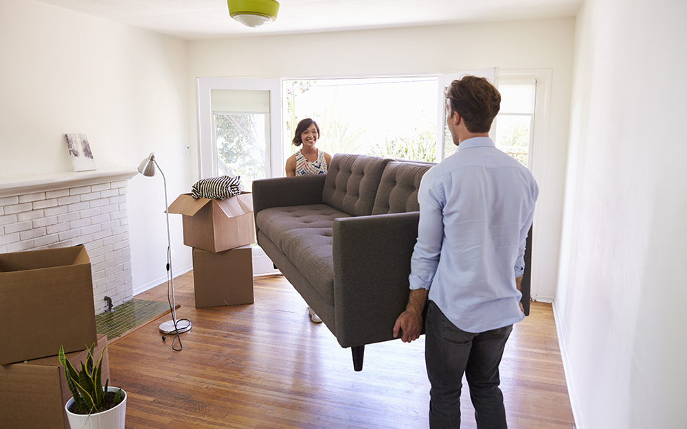 A couple moving their new sofa bed into a room.