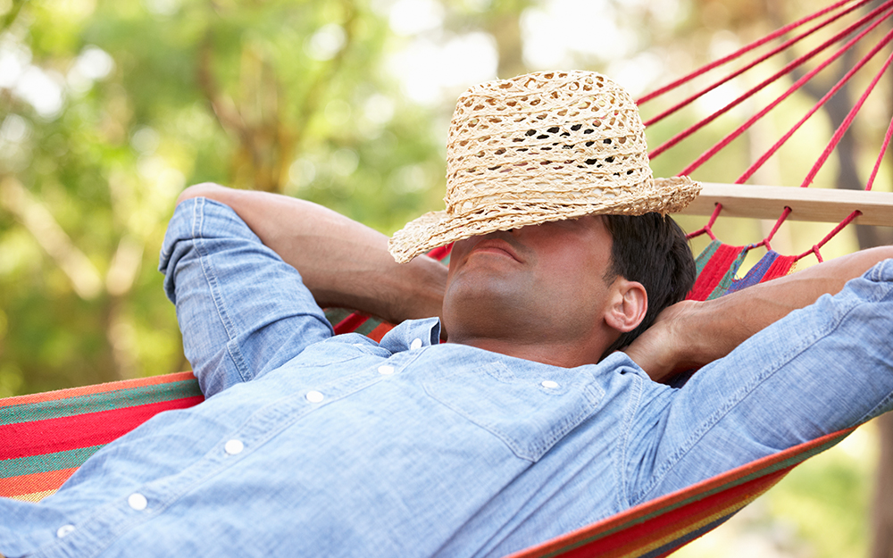 A man napping on a hammock outside with a straw hat over his eyes