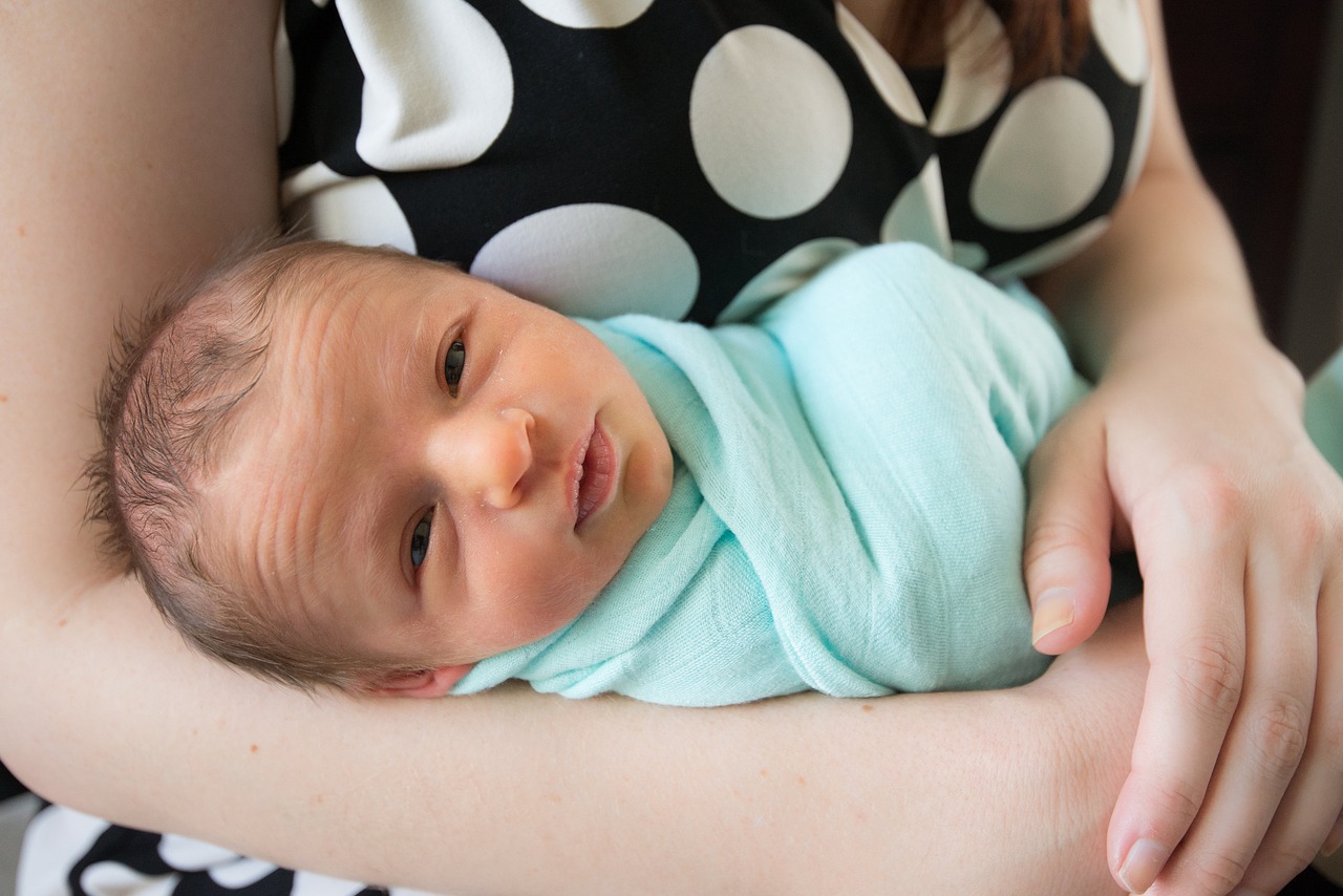 A baby, just waking up, in her mother's arms.