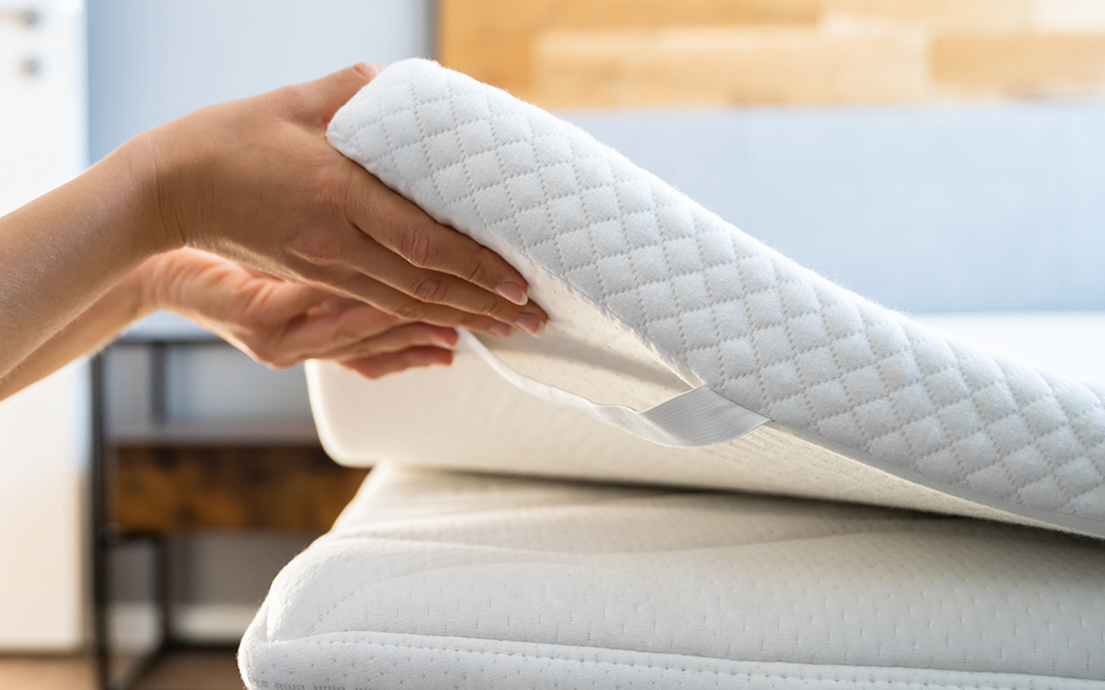 A person placing a foam mattress topper on a mattress.