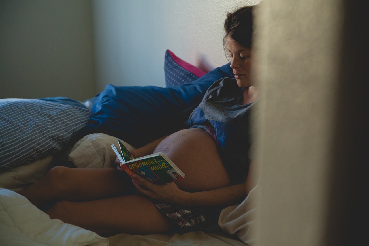 Picture of a pregnant lady looking tired and reading a book.