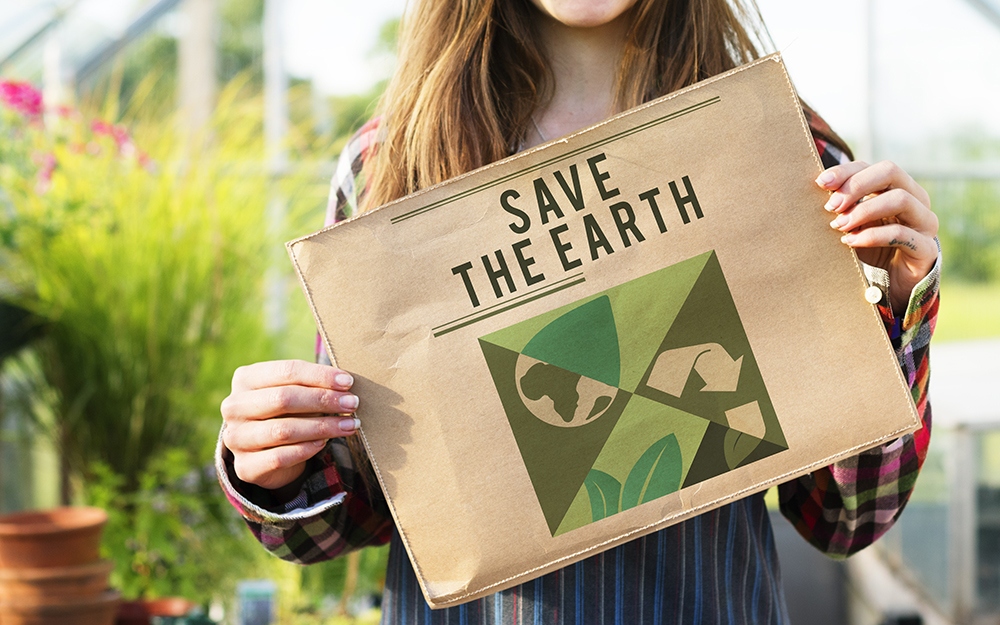 A woman holding a 'Save the Earth' newspaper in a greenhouse.