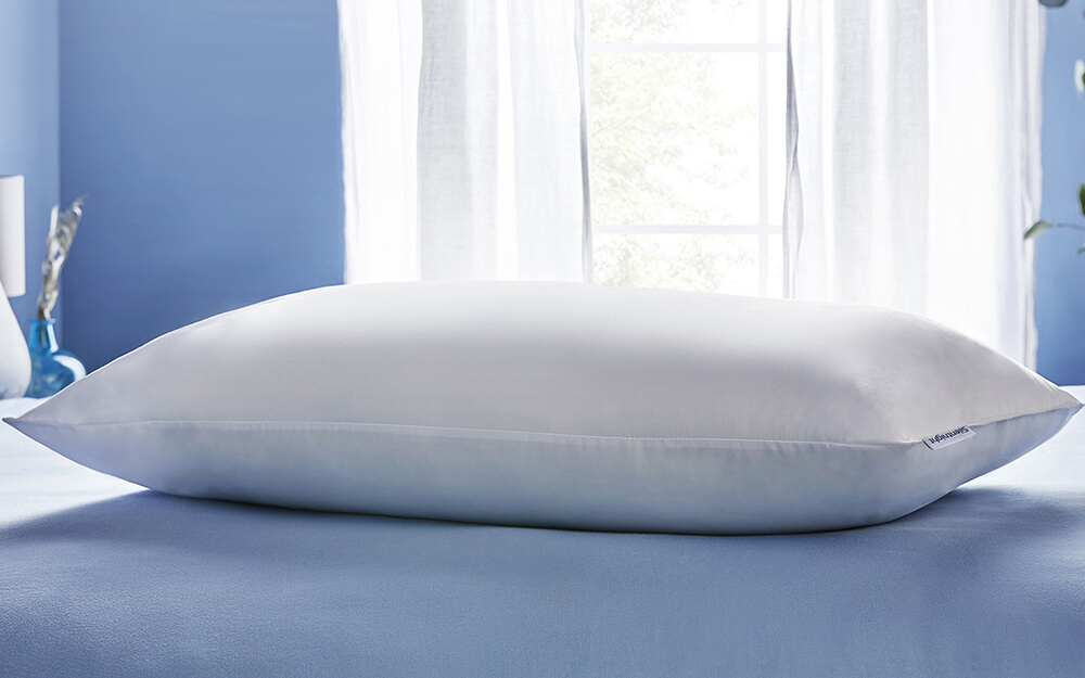 A close up of a Silentnight Anti-Snore Pillow on a bed in a blue bedroom with a window in the background.