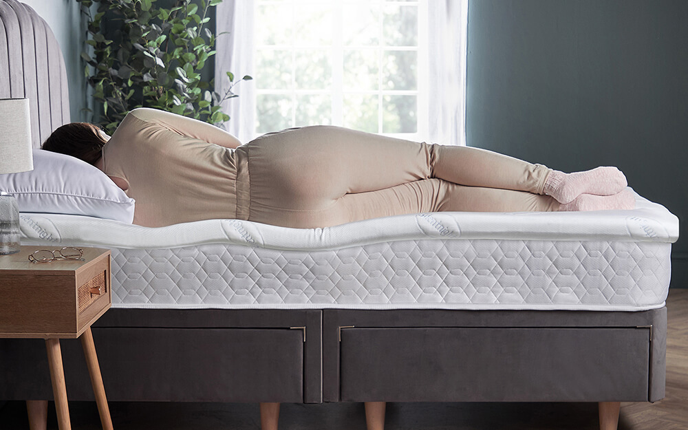 A woman sleeping on her side on a Silentnight Impress Memory Foam 2.5 Mattress Topper