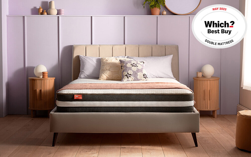 The Silentnight Just Snug Memory Hybrid Mattress on a fabric bed frame in a purple bedroom.