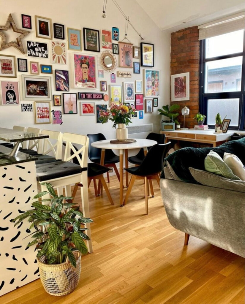 A sofa and kitchen table in a decorated room with lots of picture frames on the wall and a desk next to the window.