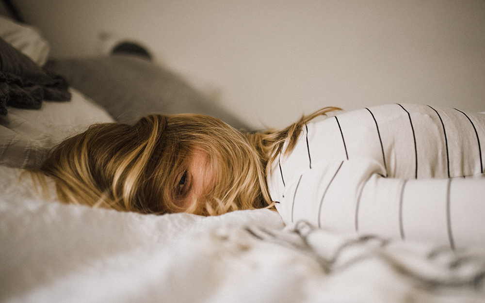 A tired woman laying on her bed with her hair covering her face.