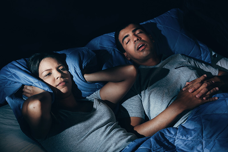 Woman covering ears with pillow as partner snores