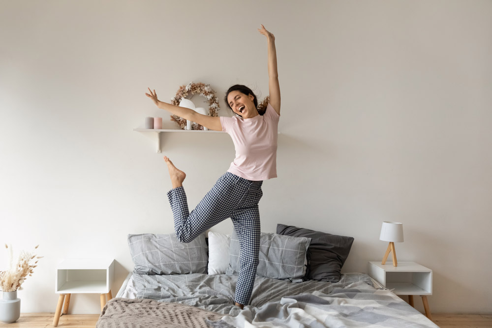 Woman dancing on her bed in a tidy room