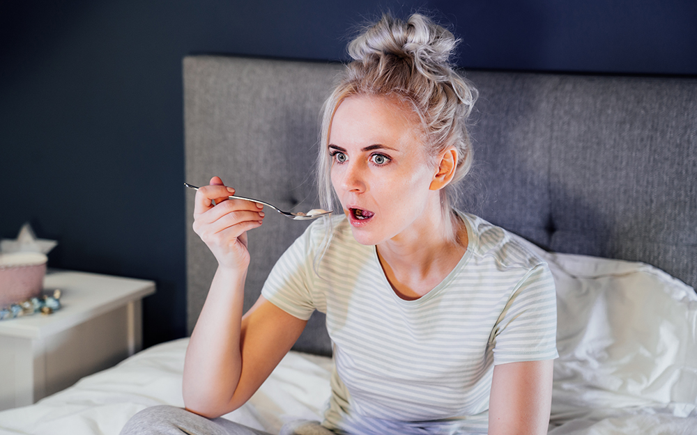 Woman eating ice cream while watching TV in bed