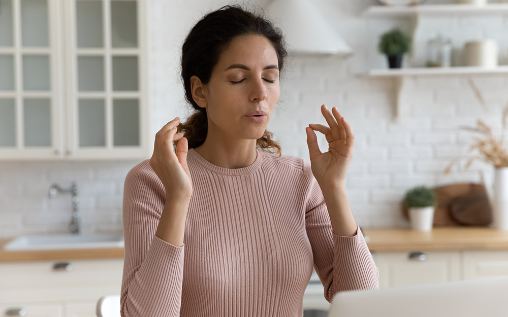 A woman sitting at a kitchen counter breathing deeply and pinching her fingers together.