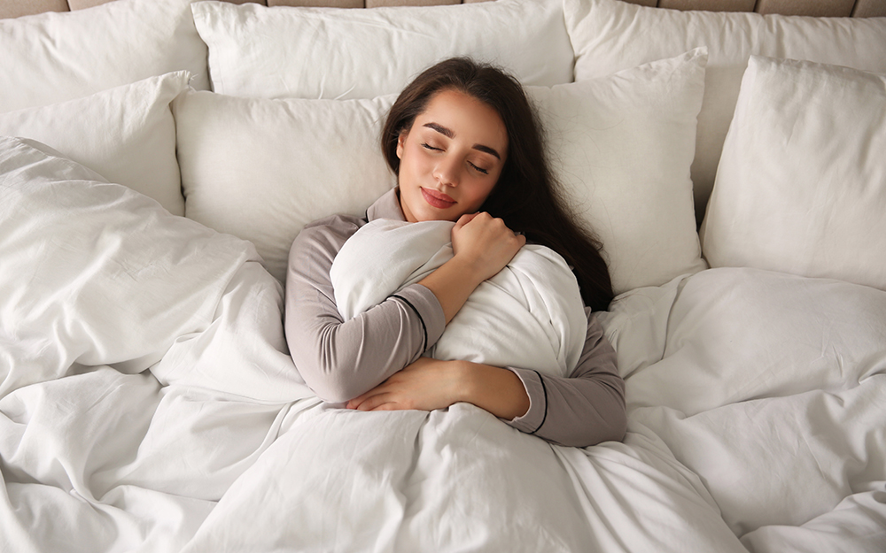 A woman sleeping on her back, hugging a white duvet