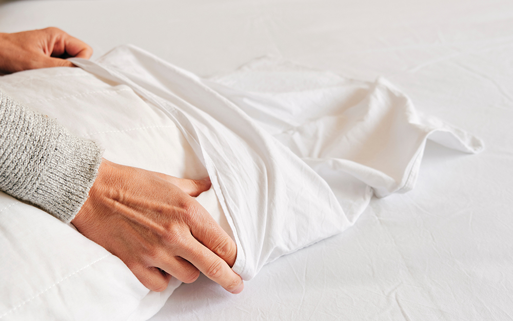 A woman putting a pillowcase over a pillow