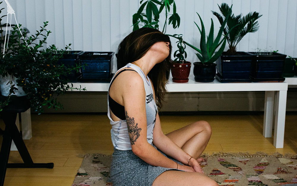 A woman sat cross-legged on the floor stretching her neck.