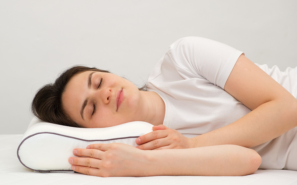 A woman laying on her side on a memory foam pillow smiling