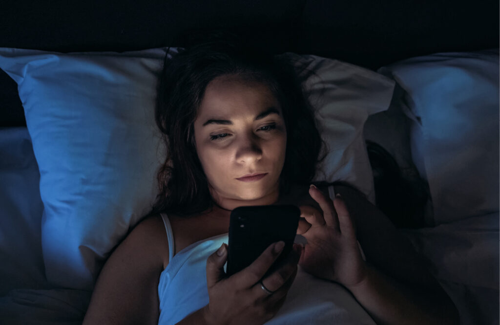 Woman using social media on phone in bed at night